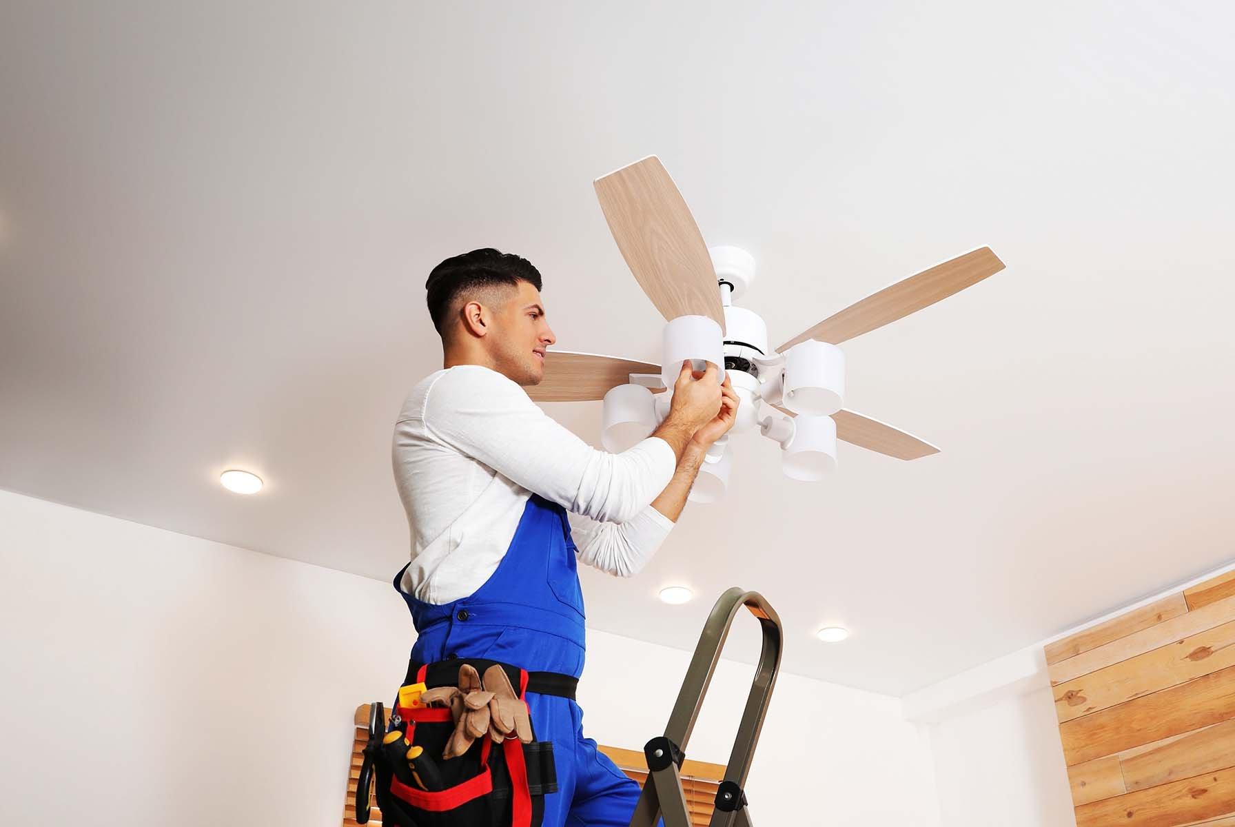 Man on ladder installing a ceiling fan.